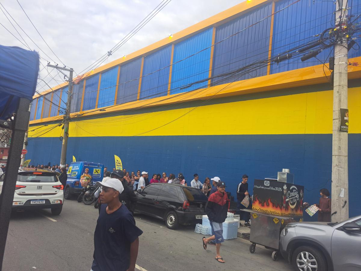 Fila de clientes para inauguração do X Supermercados no Cocaia contorna o quarteirão e alcança o final da Rua Ilha Comprida, movimentando intensamente a região desde as primeiras horas da manhã.