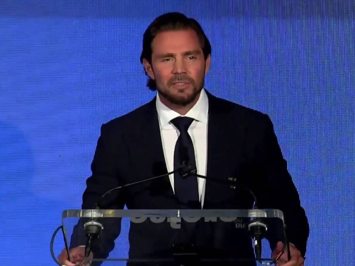 Homem de cabelos escuros e barba curta veste terno preto, camisa branca e gravata preta, falando em púlpito transparente com microfones, fundo azul.Homem de cabelos escuros e barba curta veste terno preto, camisa branca e gravata preta, falando em púlpito transparente com microfones, fundo azul. Daniel Vorcaro durante evento no ano passado em Nova York